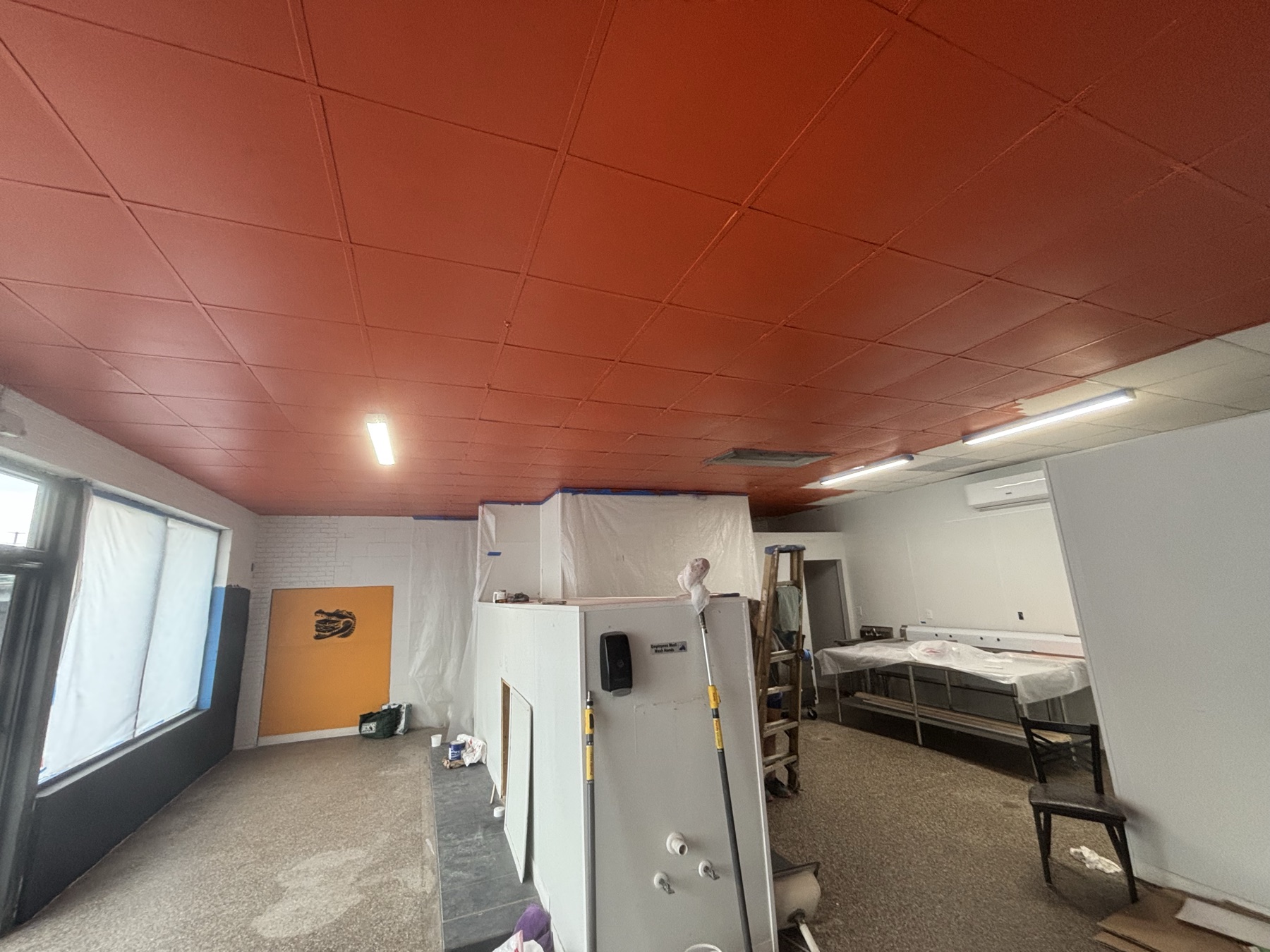 The room mid-build with the suspended ceiling painted deep orange, walls still bare block, and an orange door at the far end.
