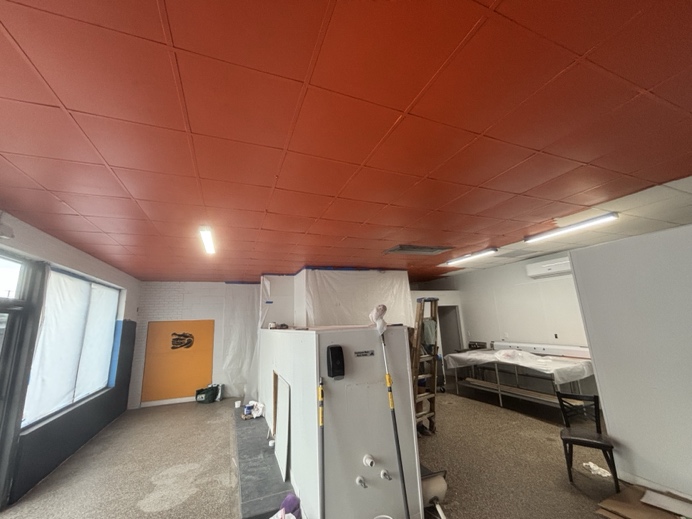 The room mid-build with the suspended ceiling painted deep orange, walls still bare block, and an orange door at the far end.
